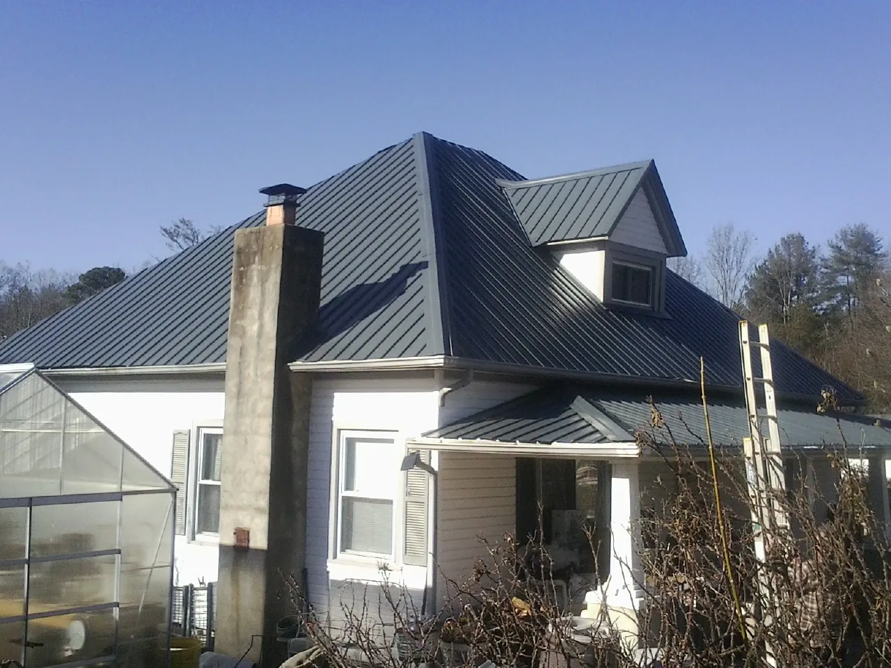 Dark blue standing seam metal roof on a white farmhouse with dormer — Slate & Tile Roof Repair by Roofing Brothers in Luna Pier