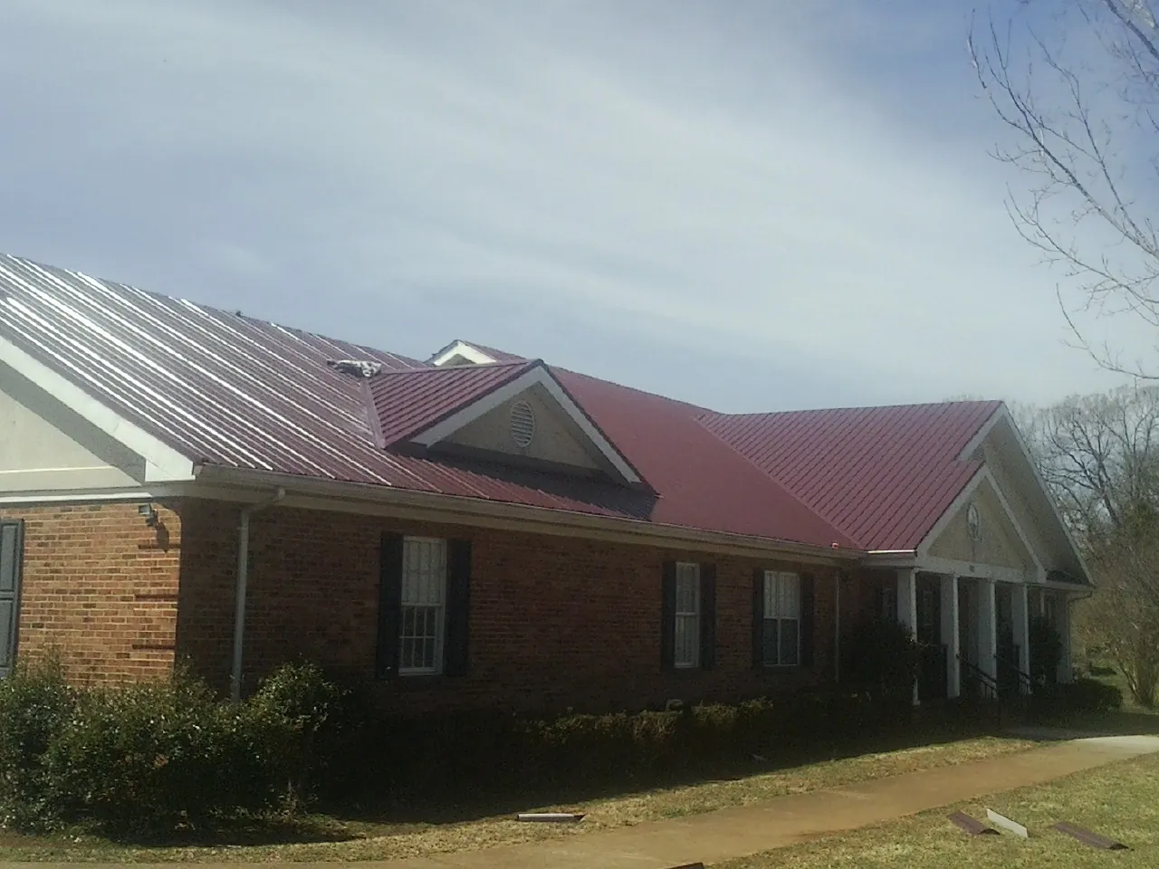 Red metal roof with gabled entries on a long brick building, from a Hail Damage Roof Repair job in Luna Pier
