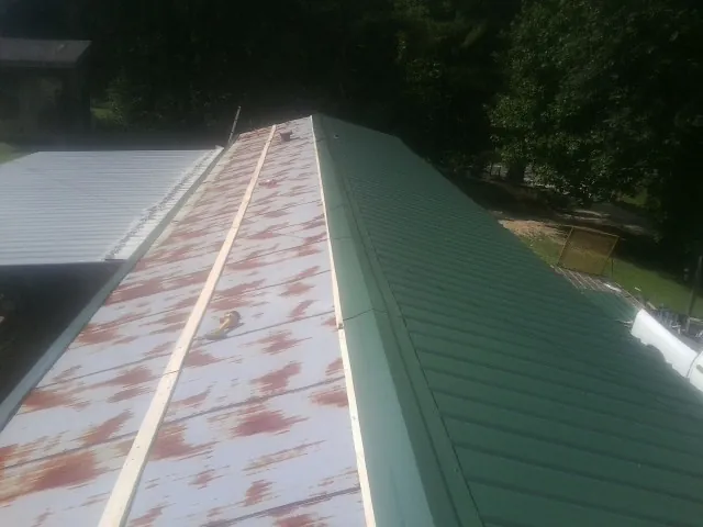Old rusted panels beside newly installed green metal roofing — Wind Damage Roof Repair by Roofing Brothers in Luna Pier