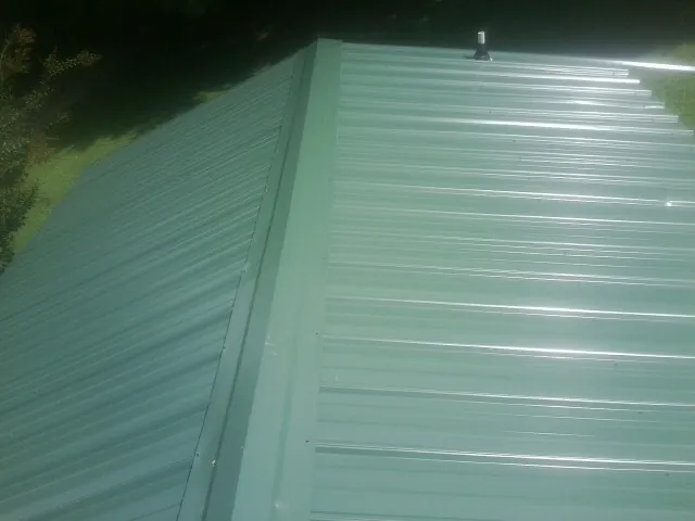 New green metal panels meeting at the ridge of a roof — Flat Roof Repair work by our crew in Luna Pier