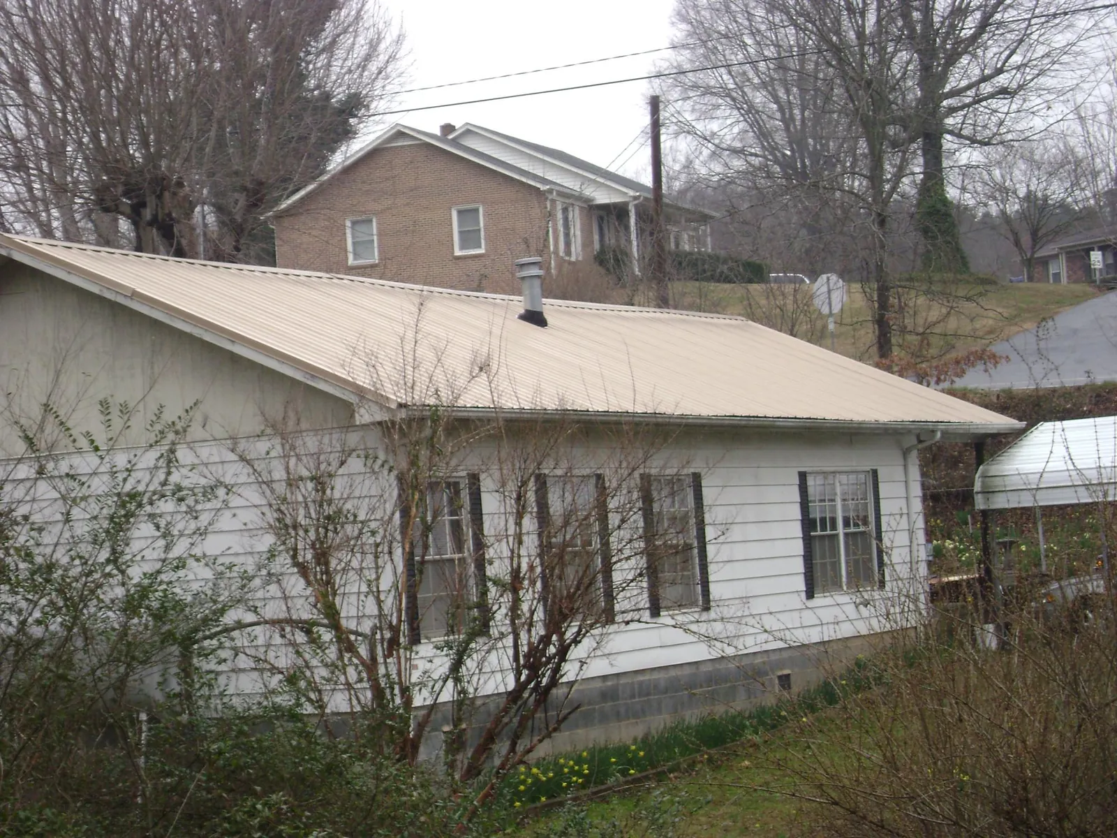 Tan metal roof on a white sided house set into a hillside — Commercial Roofing by Roofing Brothers in Luna Pier