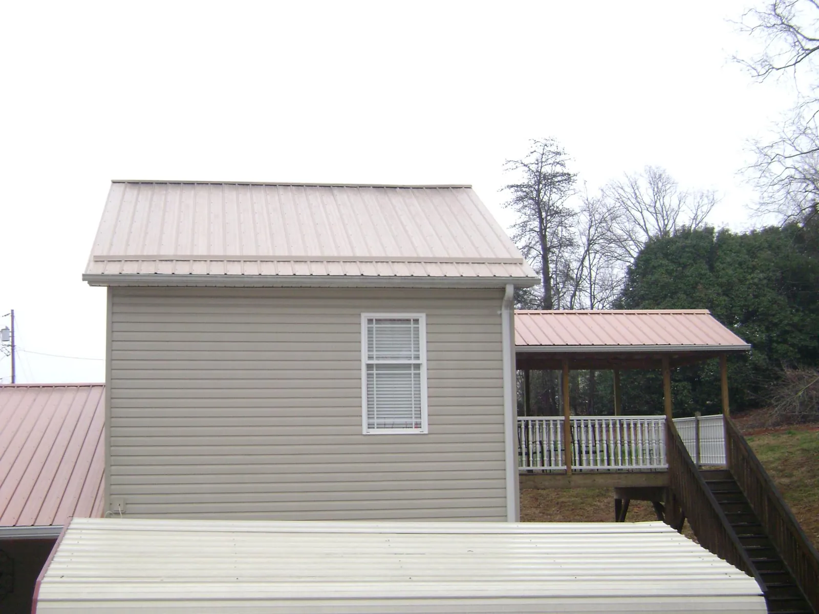 Tan metal roofs on a two story addition and attached porch, from a Roof Replacement job in Luna Pier
